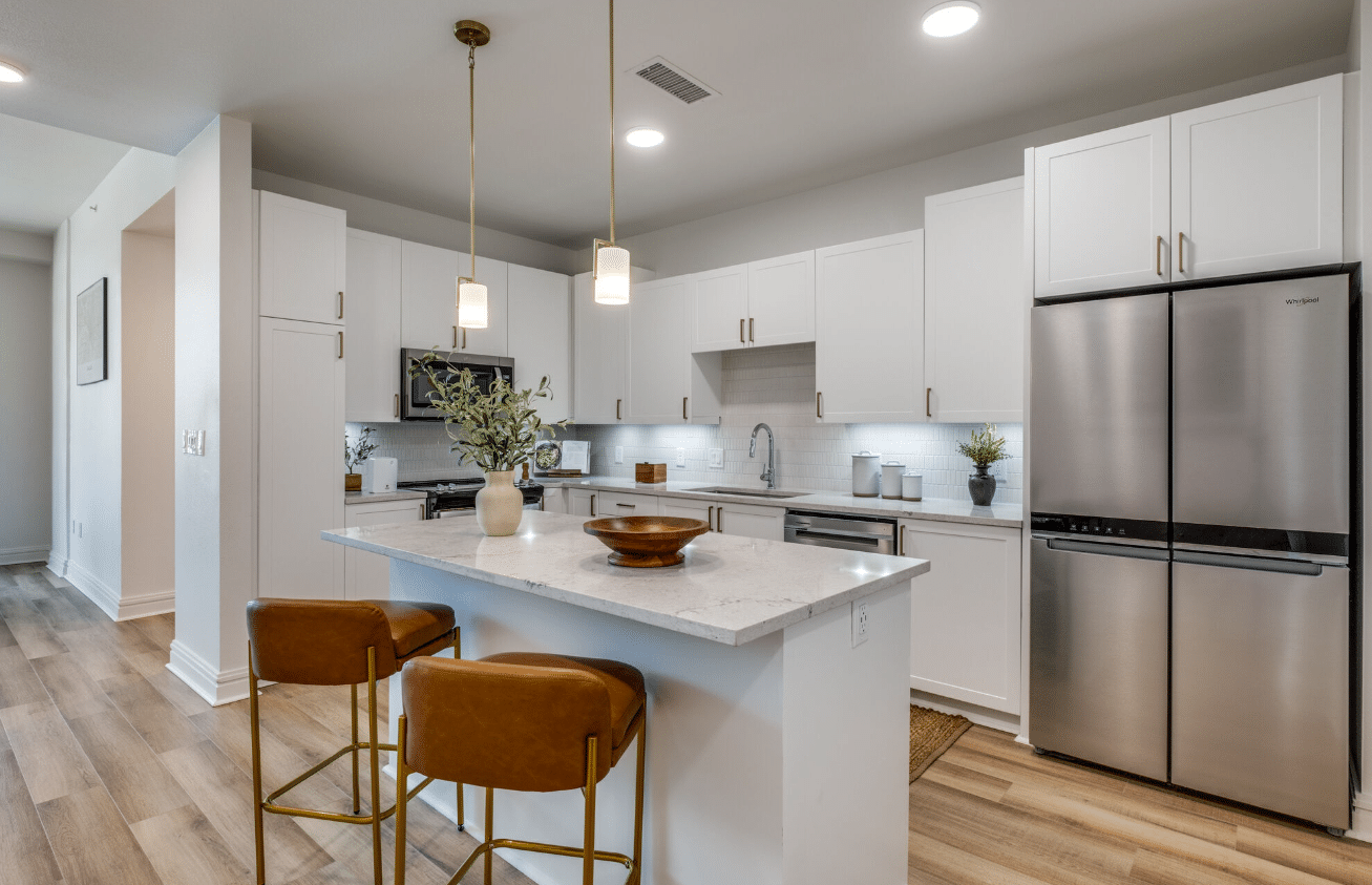 Renovated kitchen with white cabinets, stainless steel appliances, quartz countertops, and pendant lighting over a central island.
