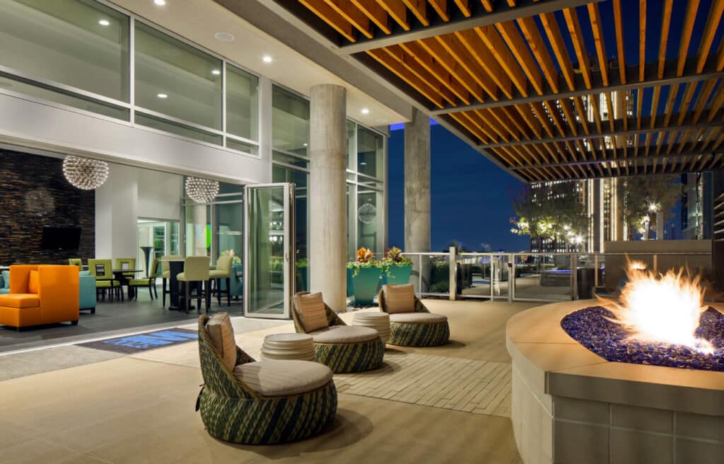Outdoor hotel lounge with fire feature, modern seating, and open-air access to the interior common area at night.