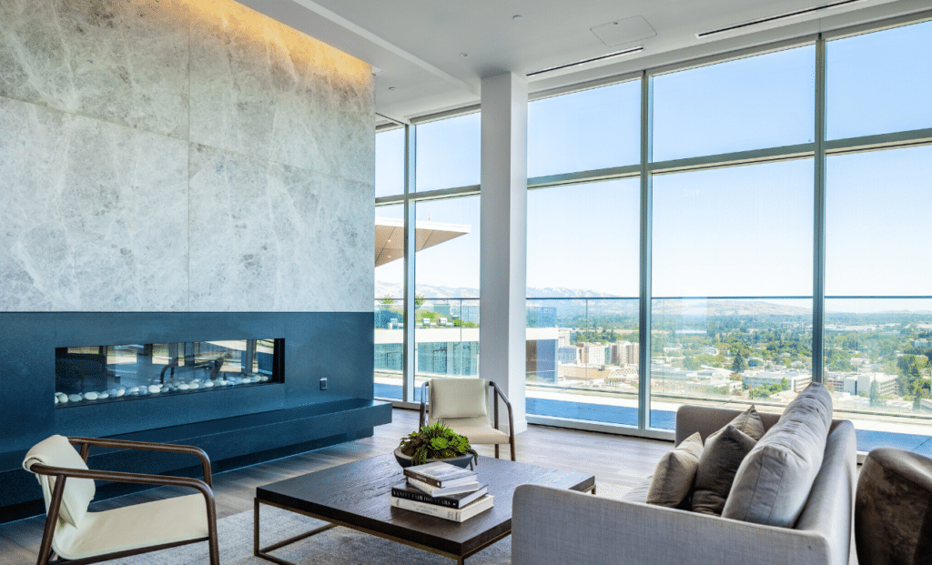 Modern high-rise living area featuring floor-to-ceiling windows, a sleek marble fireplace, and contemporary furniture with panoramic city and mountain views.