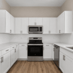 Renovated multifamily apartment kitchen featuring white shaker cabinets, quartz countertops, stainless steel appliances, and wood-look flooring.