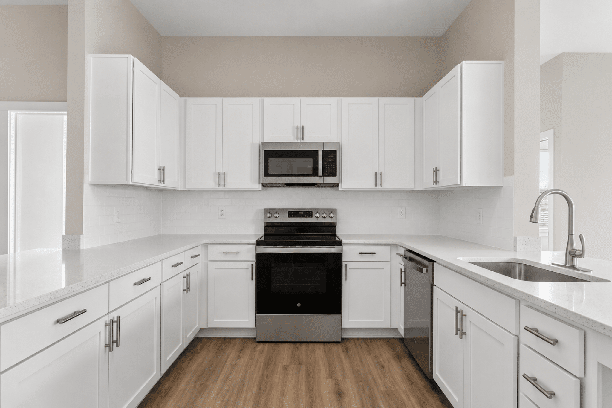 Renovated multifamily apartment kitchen featuring white shaker cabinets, quartz countertops, stainless steel appliances, and wood-look flooring.